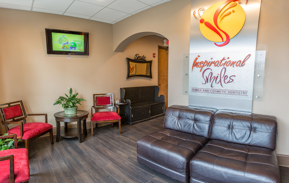 The image shows an interior space with a couch, a TV mounted on the wall, and a sign with text that reads Inspirational Smiles.