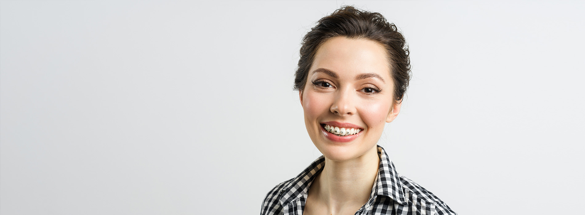A woman with short hair wearing a checkered shirt, smiling towards the camera, against a white background.