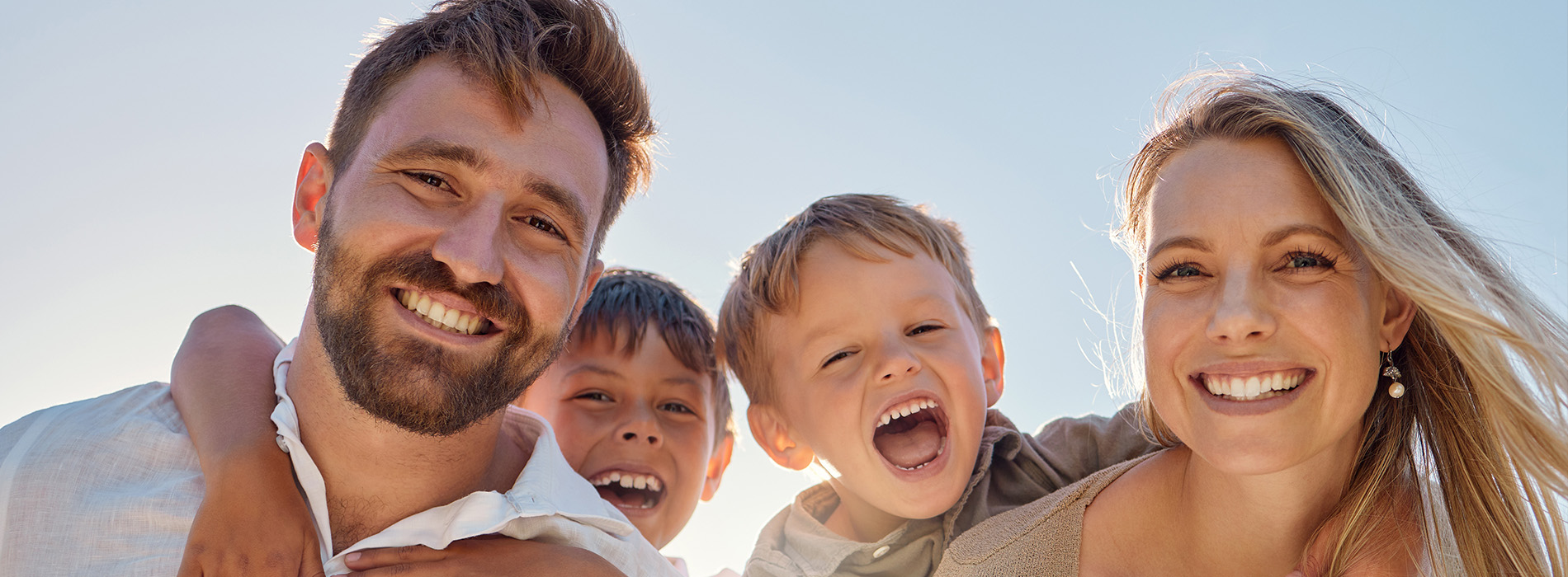 The image shows a family of four people - two adults and two children - outdoors with clear skies, smiling and posing for a photo.