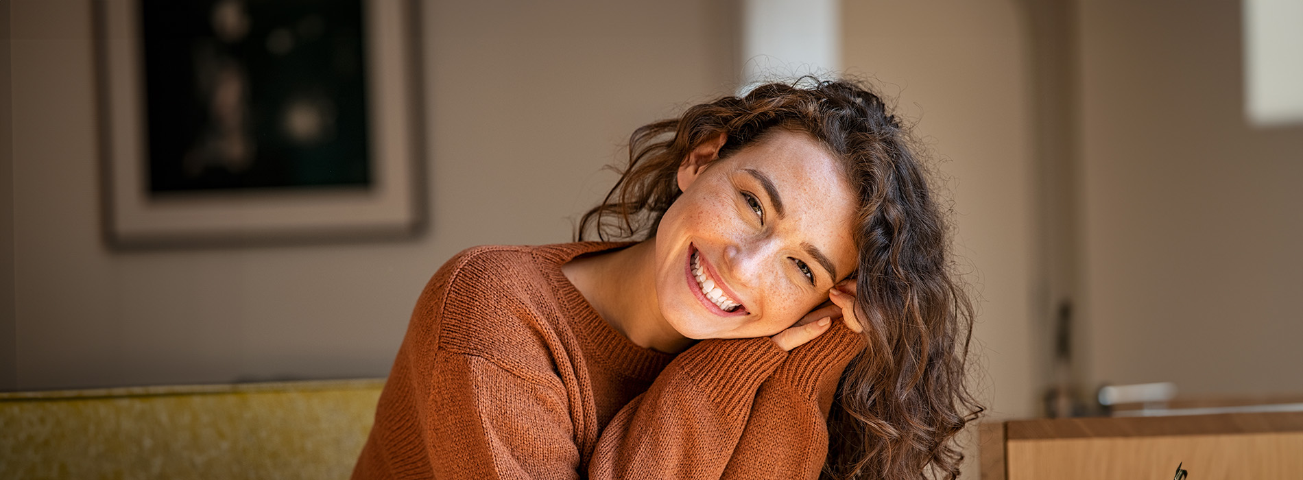 The image is a photograph of a woman with light skin, smiling at the camera. She appears to be in her late twenties or early thirties and has long hair. Her eyes are looking directly at the camera, and she is holding up her index finger near her mouth as if she s making a point or emphasizing something. The background is plain and light-colored, which suggests that this could be a stock photo used for various purposes such as advertising, personal branding, or lifestyle content.