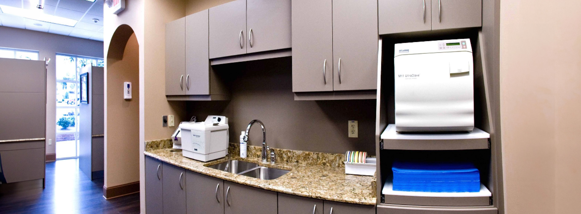 The image shows a modern dental clinic interior with various pieces of equipment, including a dental chair and an X-ray machine.