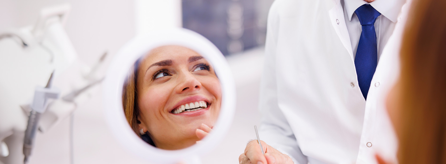A person is seated in a dental chair, receiving care from a dental professional who stands behind them.