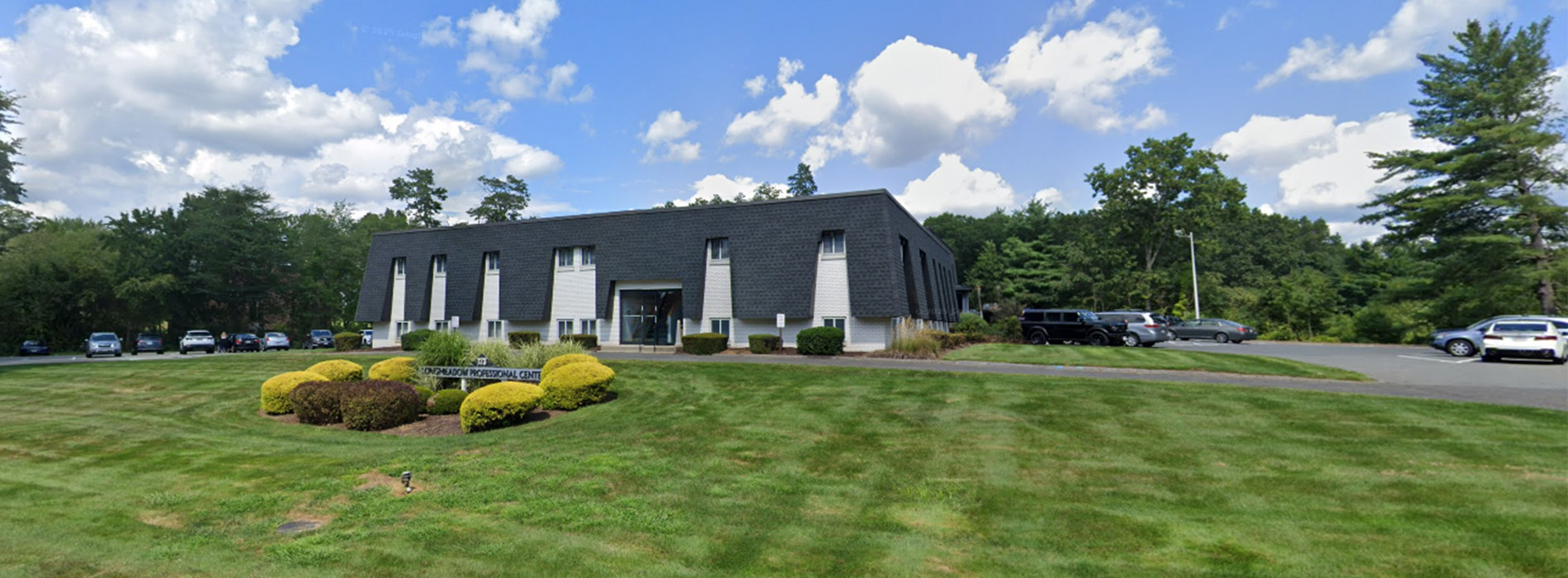 The image shows a group of people, possibly professionals given their attire and the setting that appears to be an office or professional environment. They are gathered around a table with a laptop on it, engaged in what seems to be a discussion or meeting.