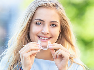 The image features a young woman holding up a toothpaste tube with a smile on her face, showcasing her teeth.