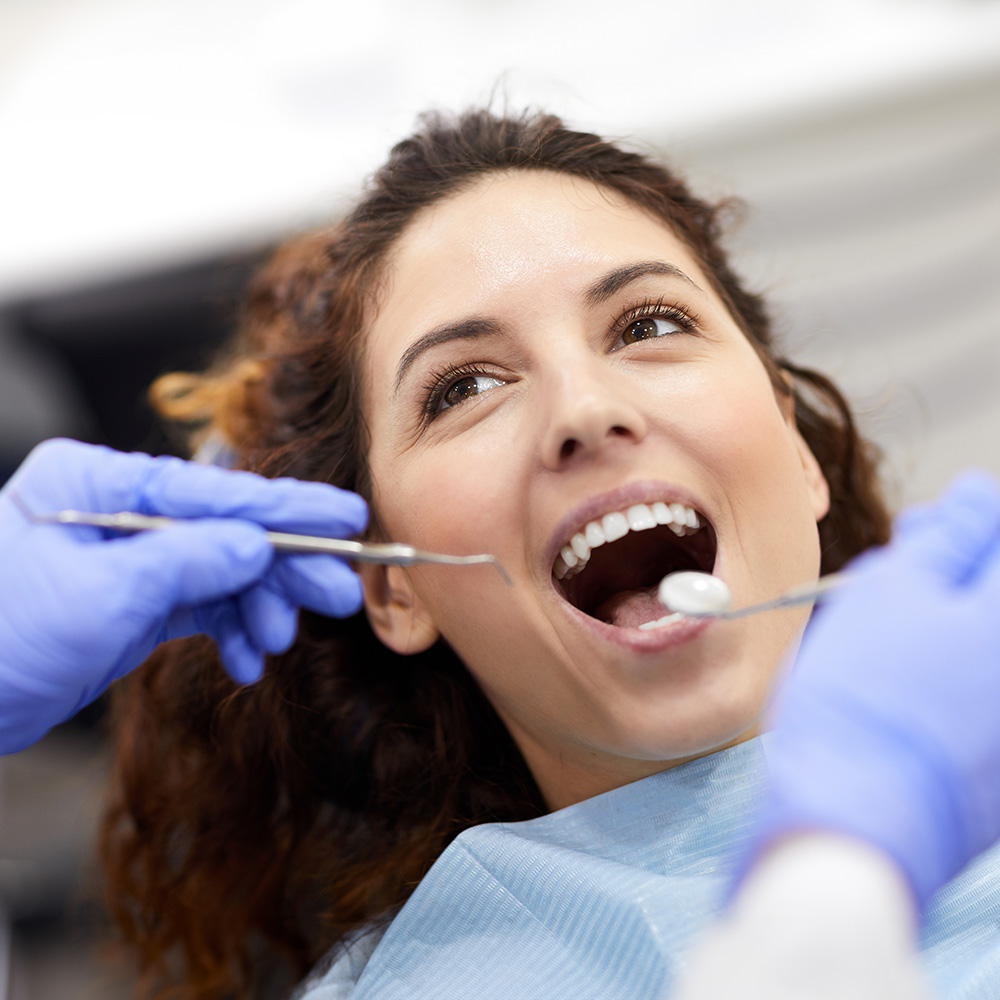 Woman wearing blue gloves holding a toothbrush in her mouth while sitting in a dental chair.
