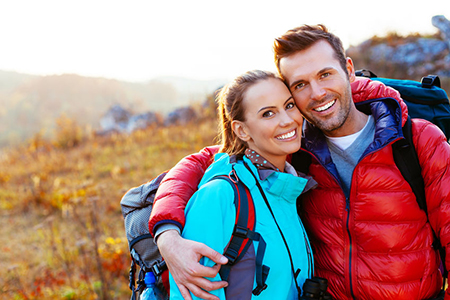 The image shows a man and a woman embracing each other outdoors with backpacks, suggesting they are hikers enjoying a moment together during their adventure.