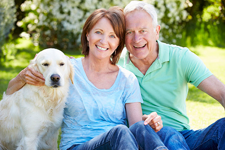 An elderly couple sitting on grass with their golden retriever dog, smiling at the camera.