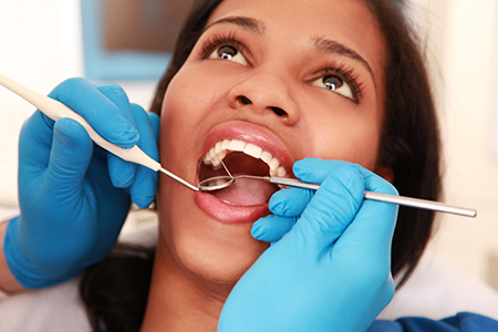 Woman receiving dental care with tools visible around her mouth.