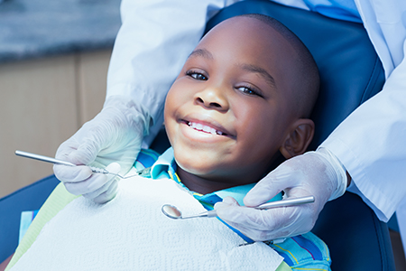 A young boy sitting in a dental chair with a smiling expression, receiving dental care from a professional who is out of frame.