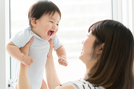 A woman holding a baby with a joyful expression while looking at the camera.
