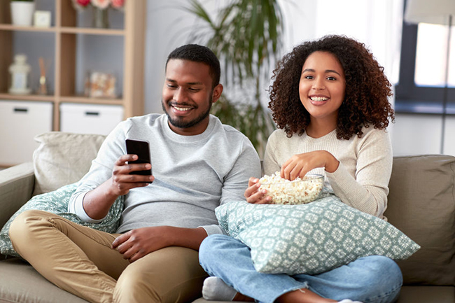 A couple sitting on a couch, sharing a moment together while enjoying popcorn.