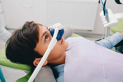 A young person lying down with an open mouth, wearing a dental device over their face, likely at a dentist s office.